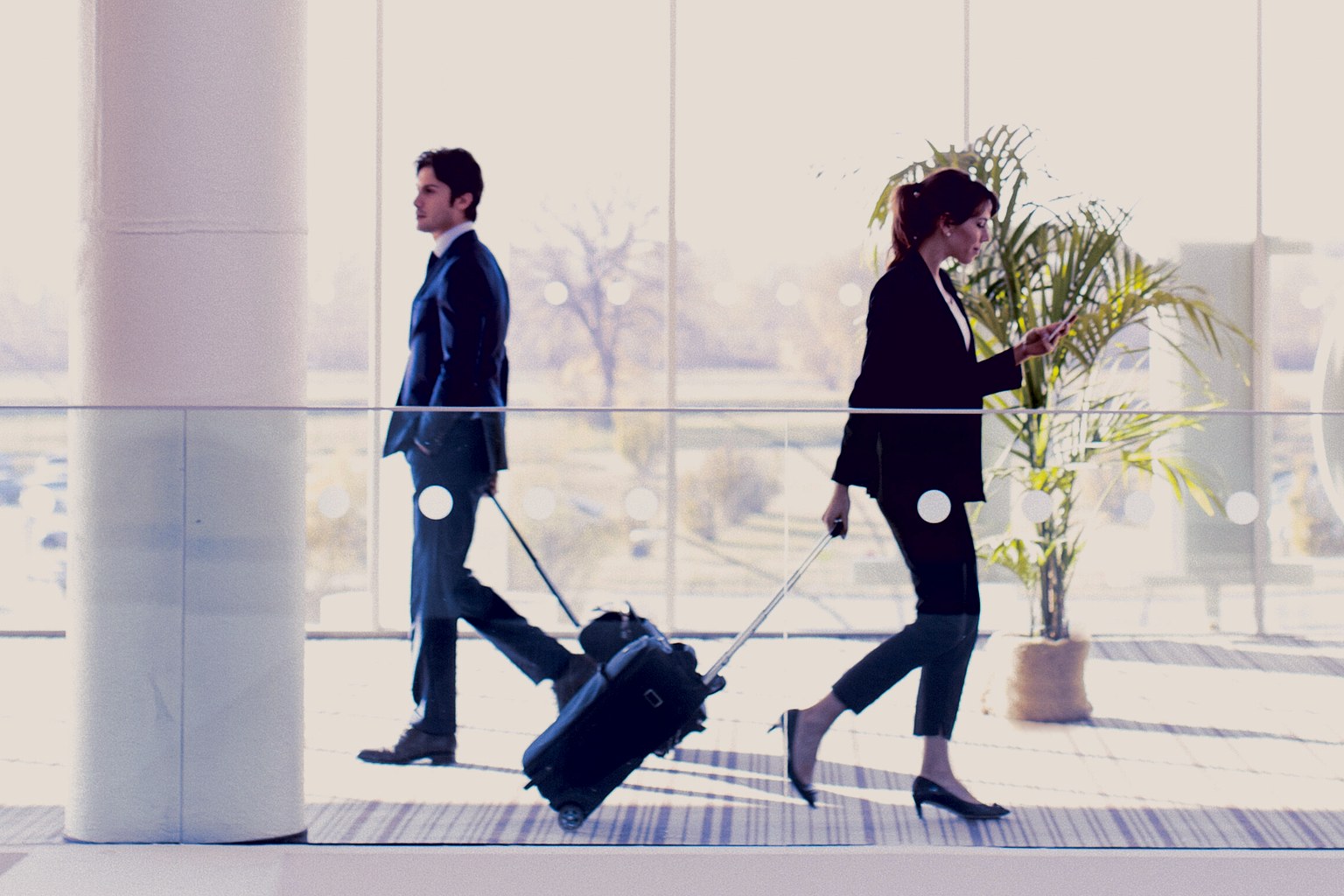 Two business travellers with luggage crossing a bright hotel concourse